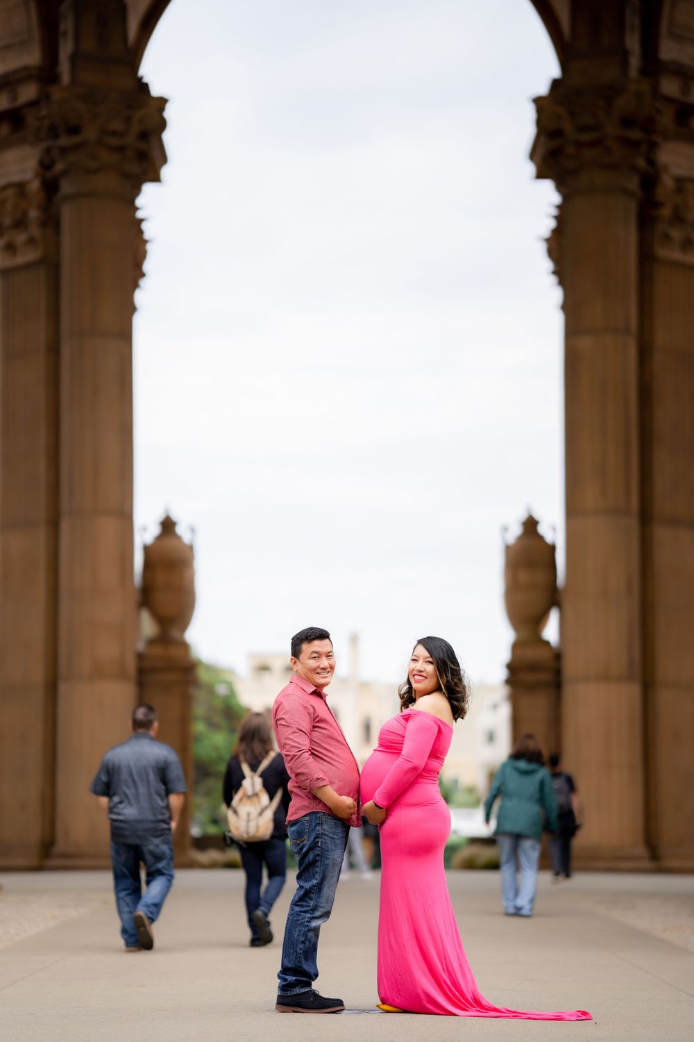 Standing under ornate stone arches with elegant architectural detail while others walk by at Palace of Fine Arts.