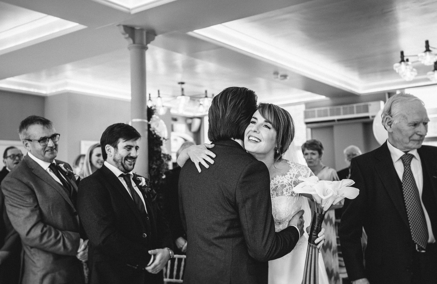 Guests share embraces during a celebration in an elegant indoor venue with columns.