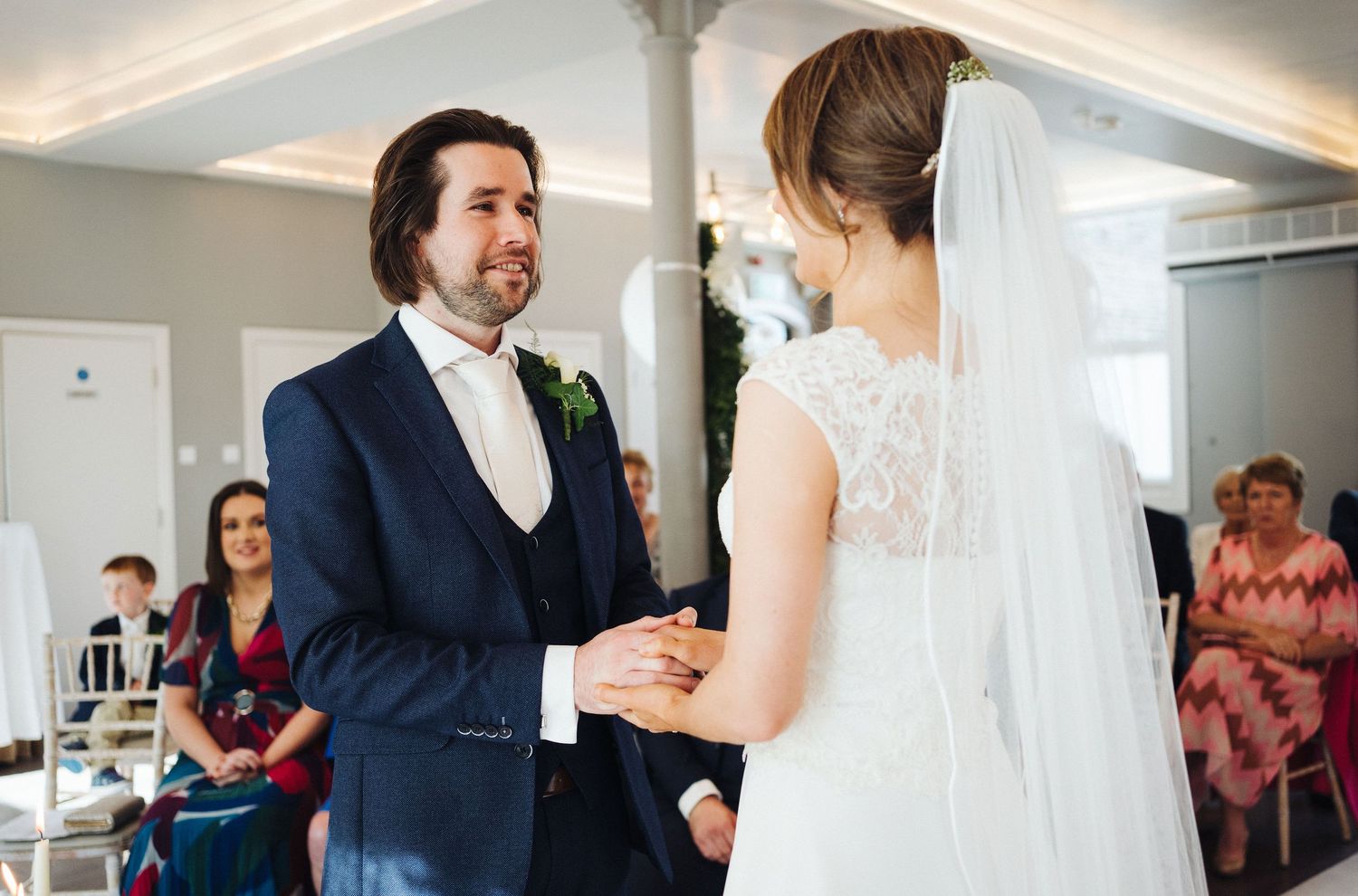 A couple exchanges vows during an indoor wedding ceremony with guests watching.