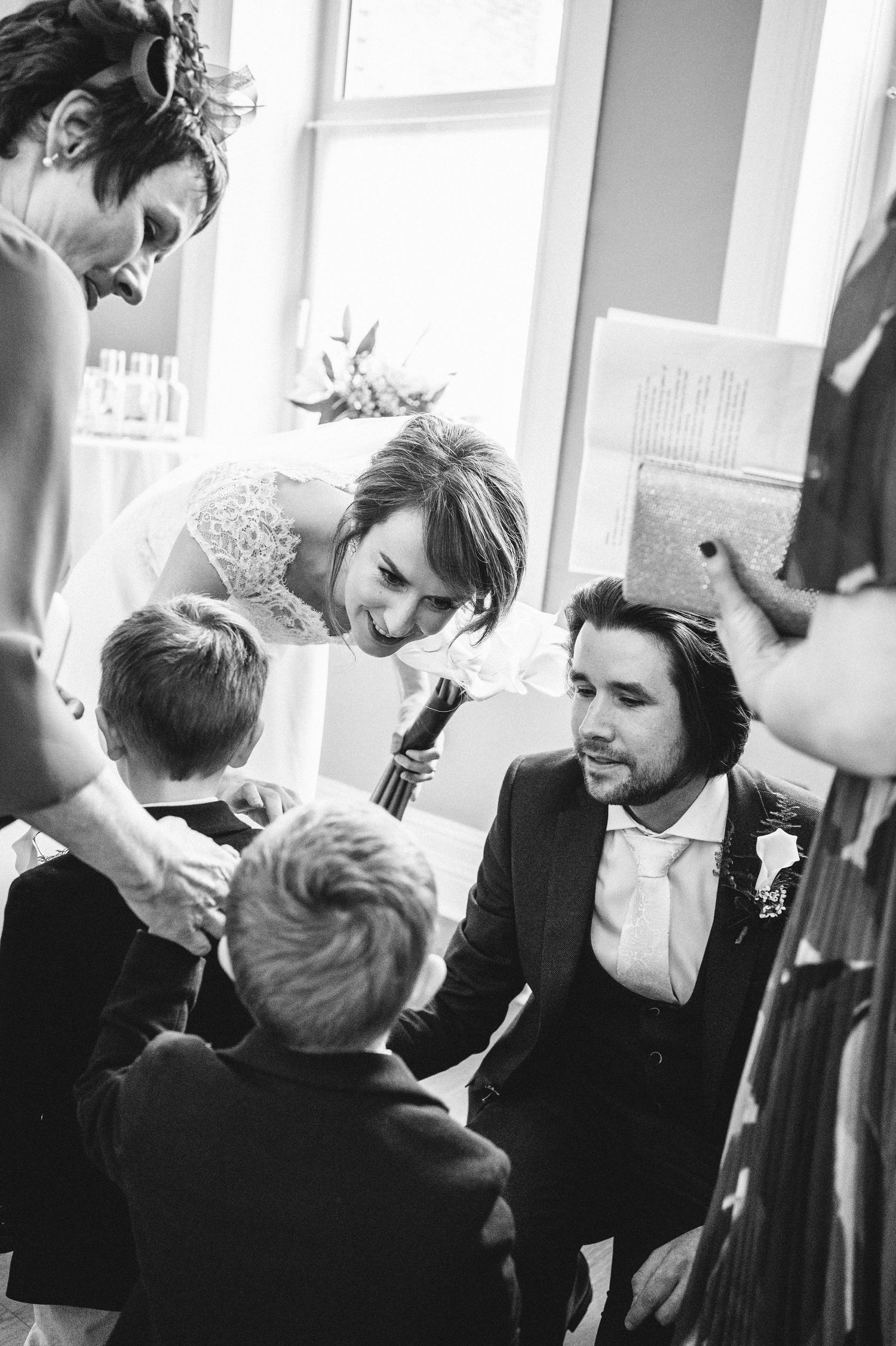 Black and white candid moment of wedding party members interacting with young children.