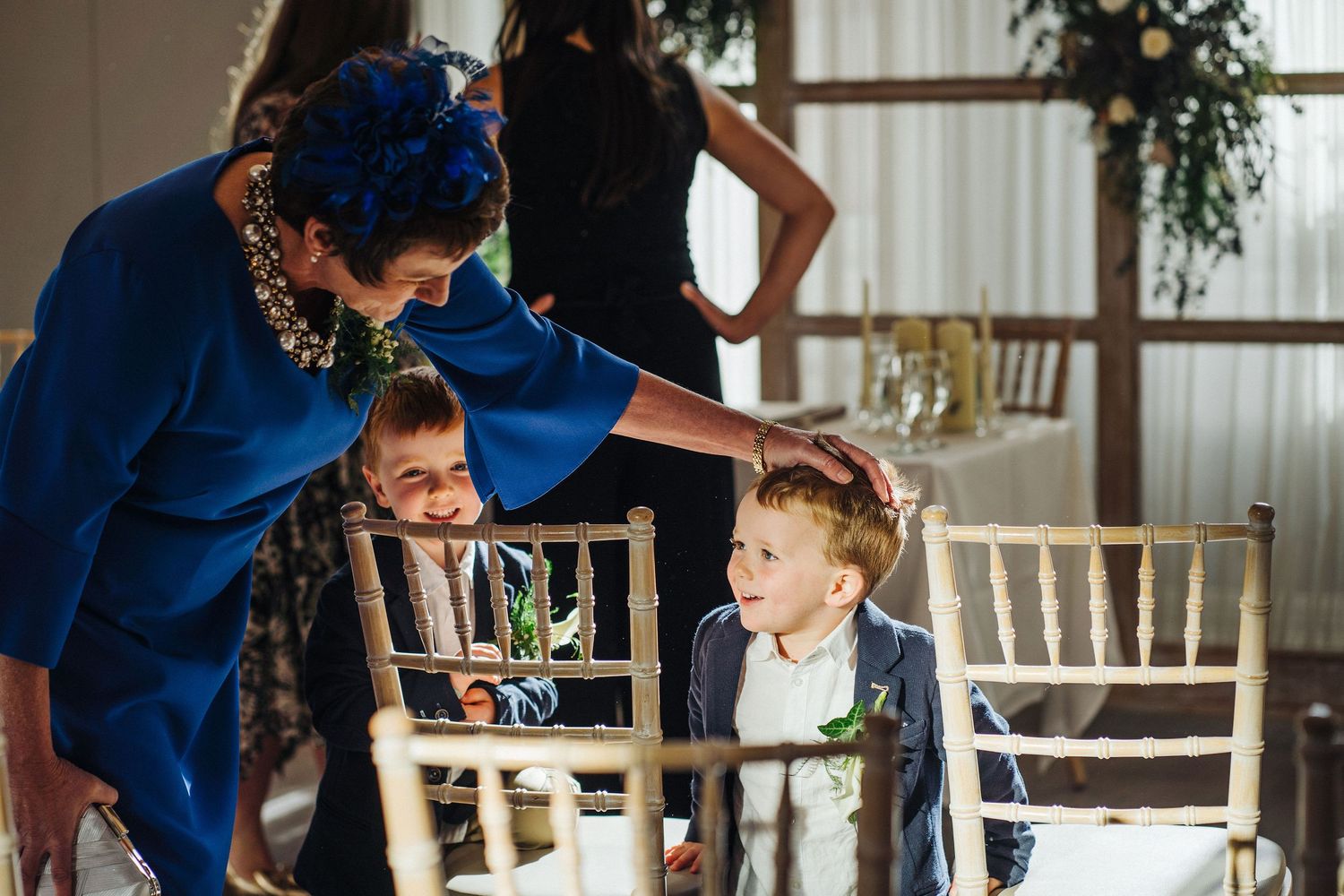 Young children at a formal event interact with an adult wearing a bright blue outfit.