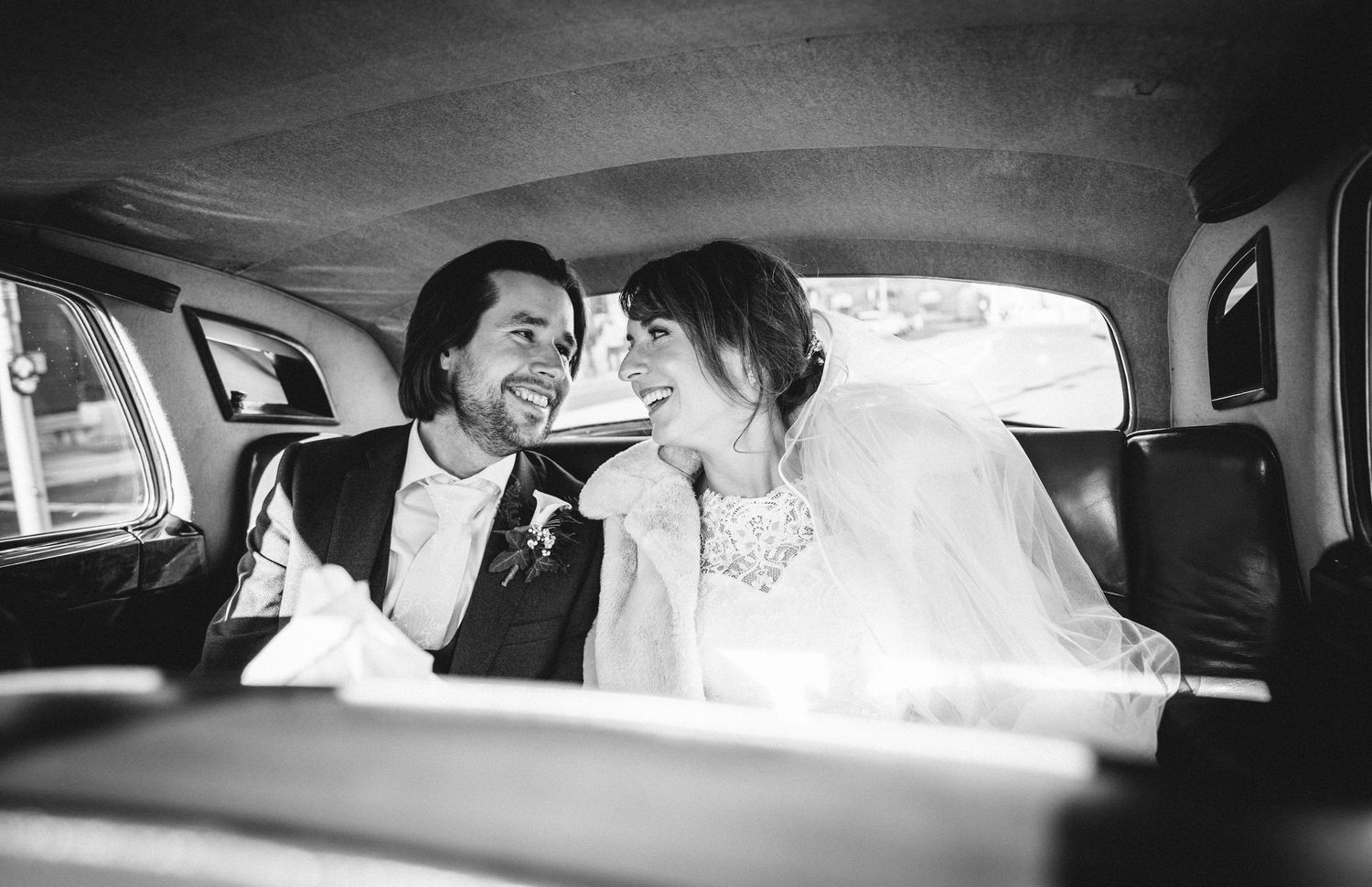 A joyful candid moment captured between two people in the back seat of a vintage car.