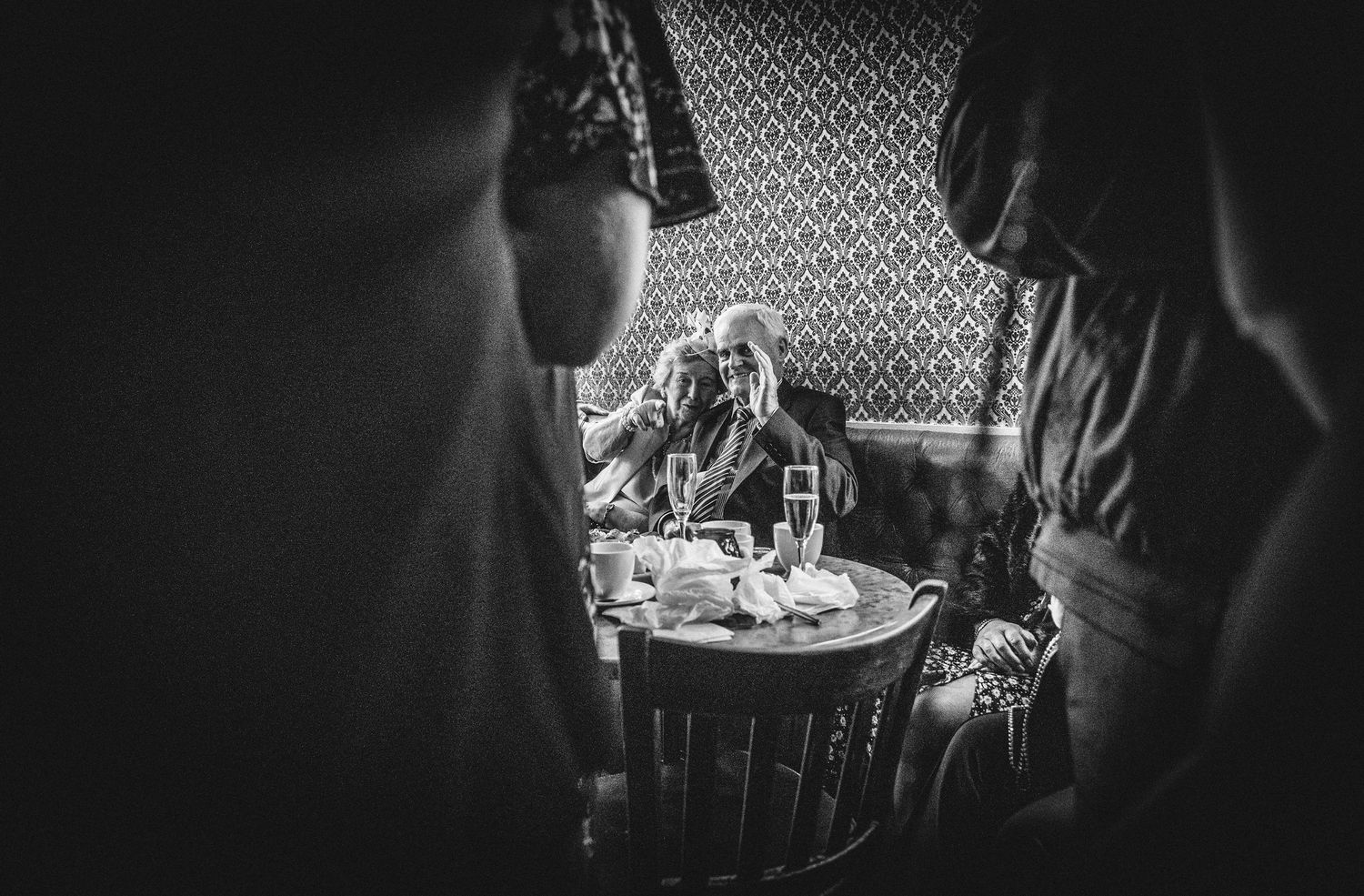 Atmospheric black and white photo of guests gathered around a table in dim lighting.