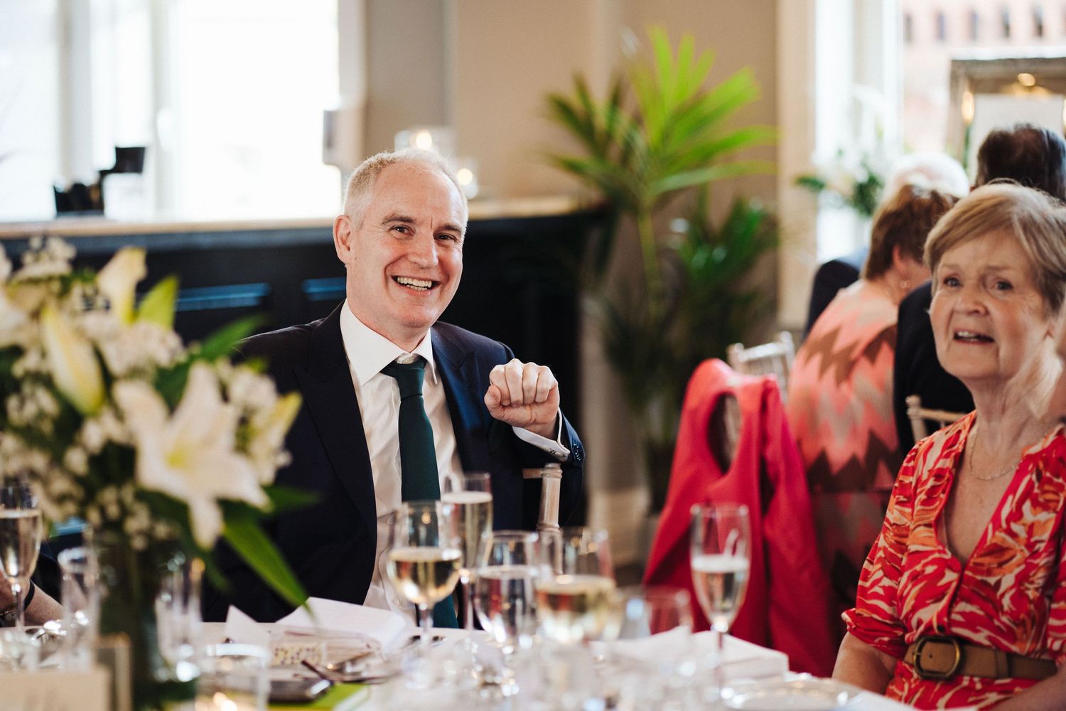 Wedding reception guests enjoying themselves at an elegant dining table with floral centerpieces.