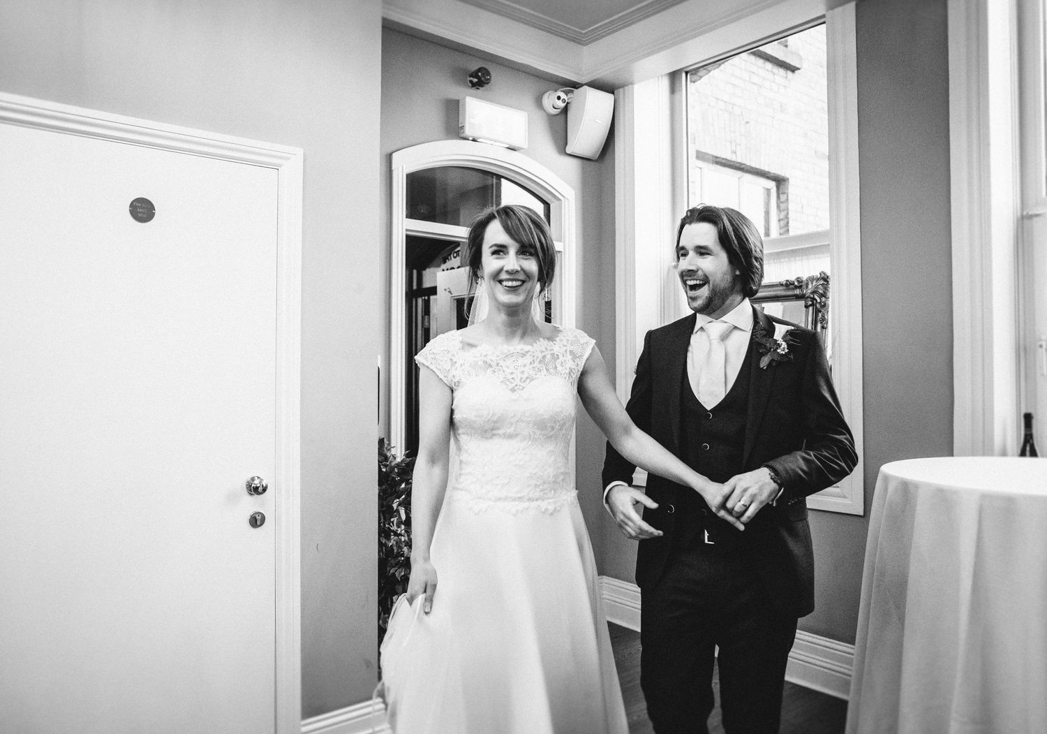 Black and white photo of a couple in formal attire walking through an elegant hallway.