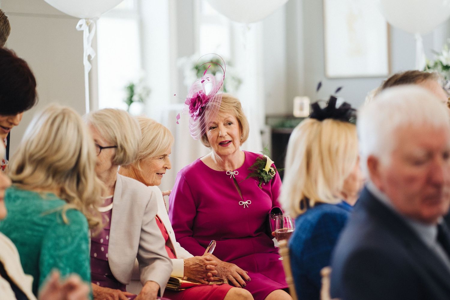 A woman in a bright fuchsia dress smiles during a formal gathering.