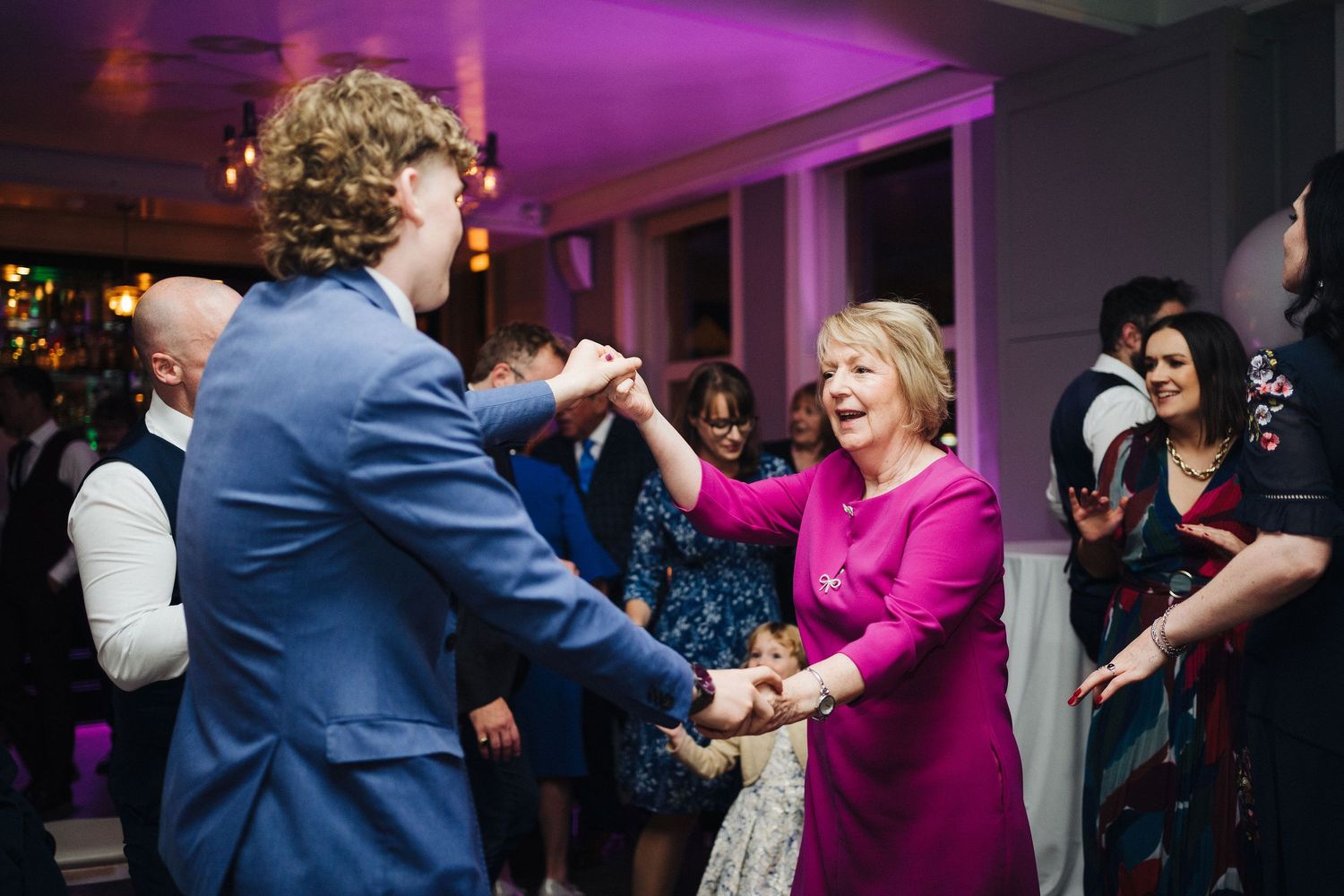 Guests sharing a spirited dance moment at an indoor celebration with purple mood lighting.