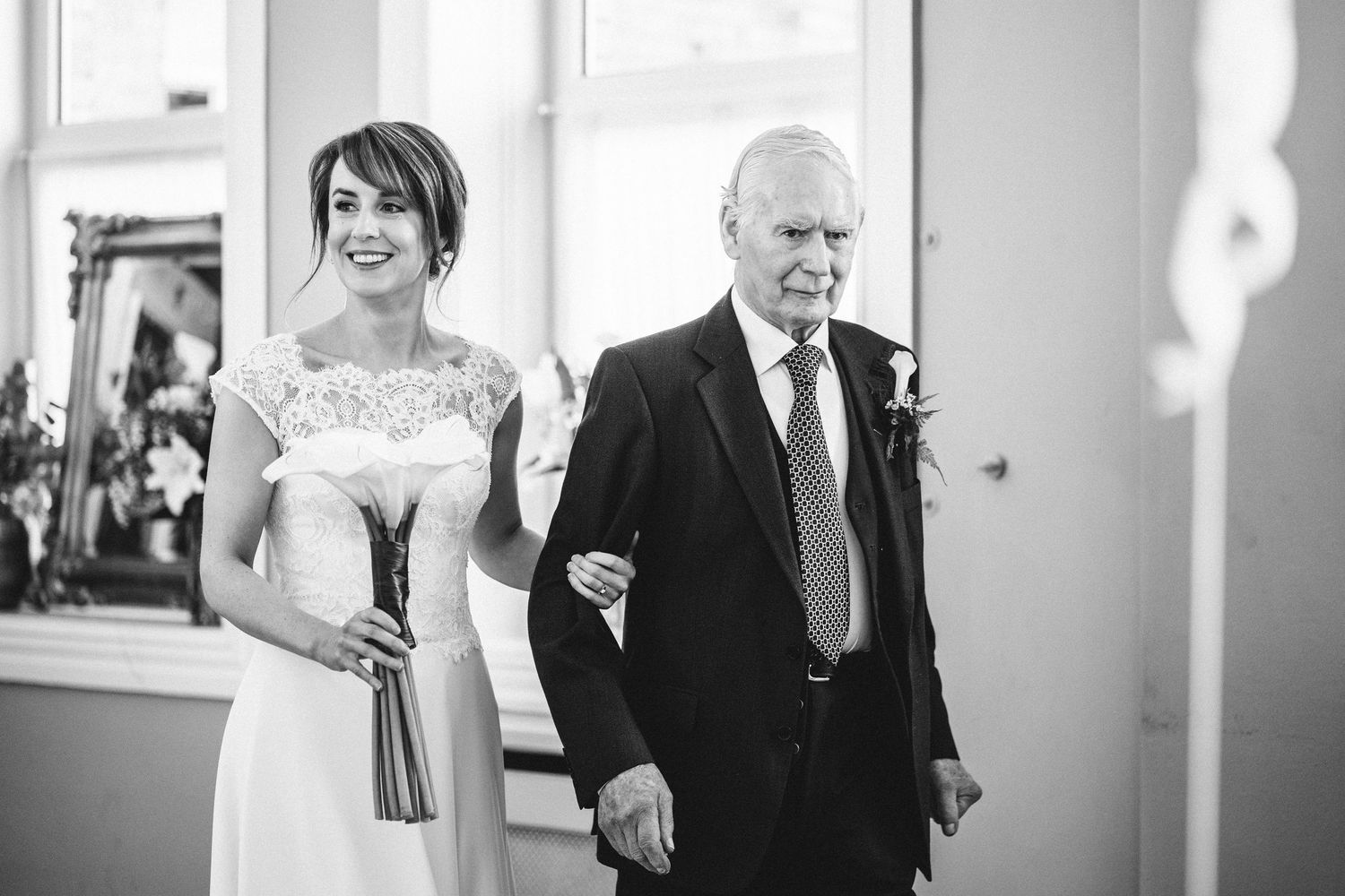 A black and white photo of a wedding processional in an elegant indoor venue.