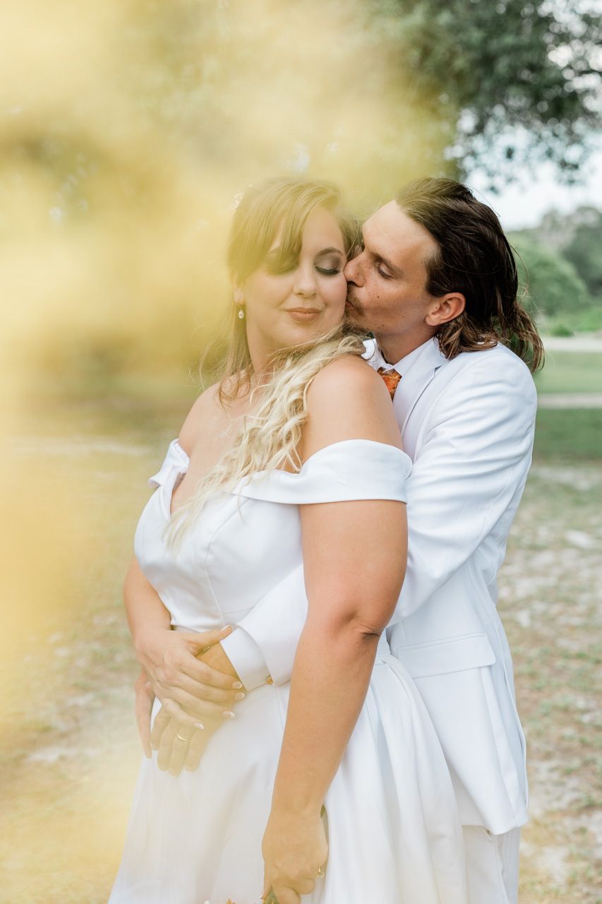 A romantic couple in white outfits embracing outdoors with a dreamy golden light effect.