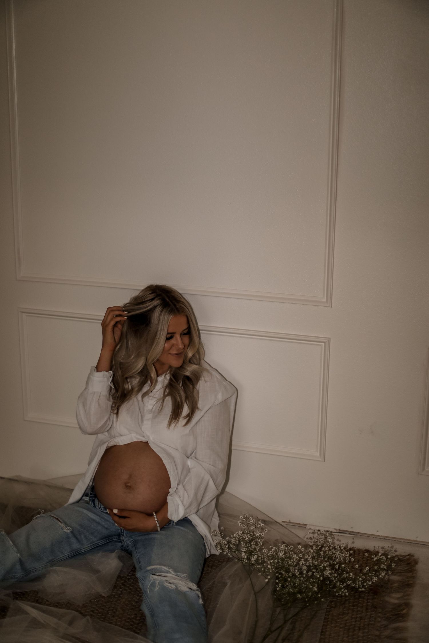 Candid maternity moment with white button-down shirt and scattered baby's breath flowers.