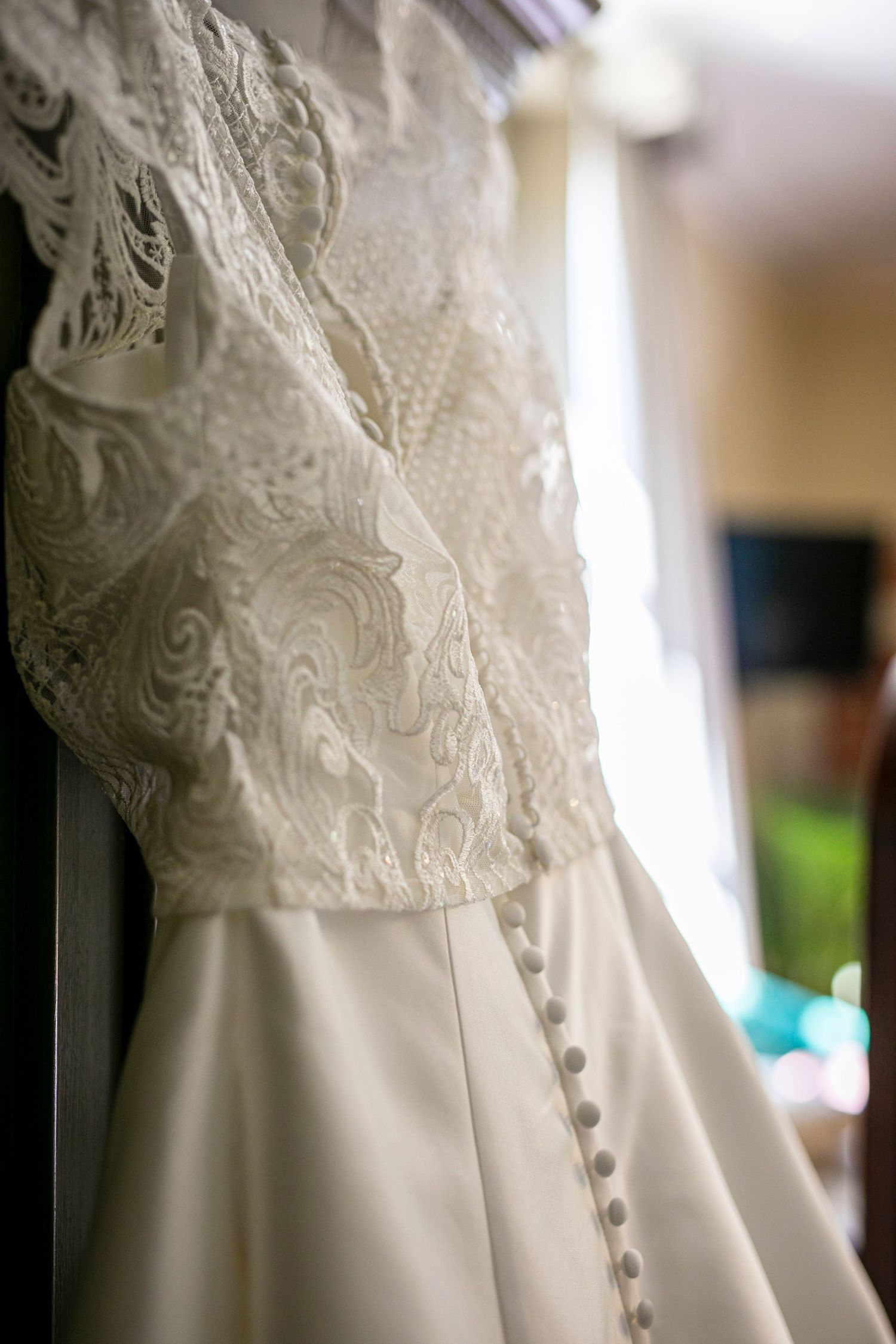 Close-up details of delicate lace and buttons on a white wedding dress.
