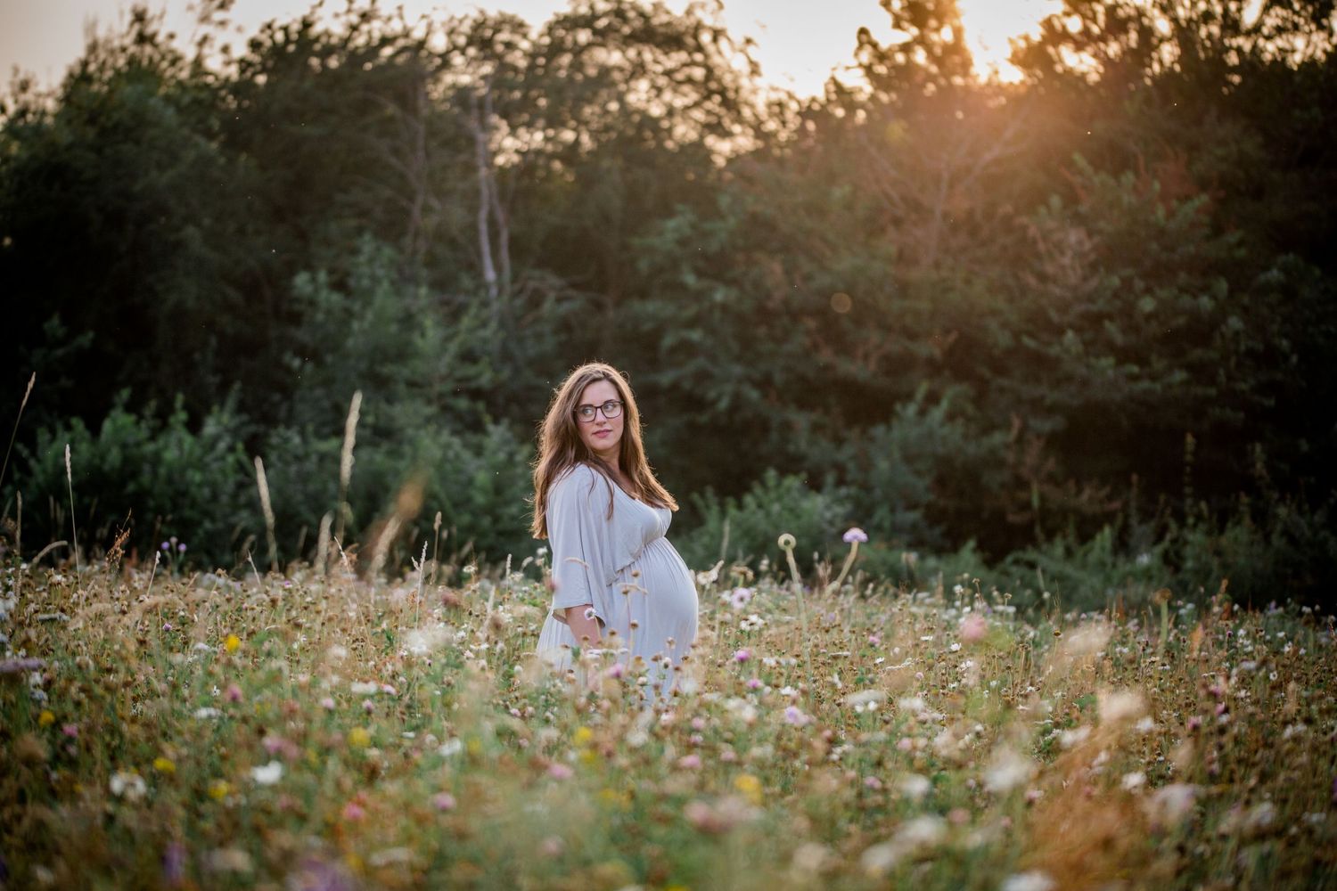 Pregnant woman standing in a flower meadow at sunset