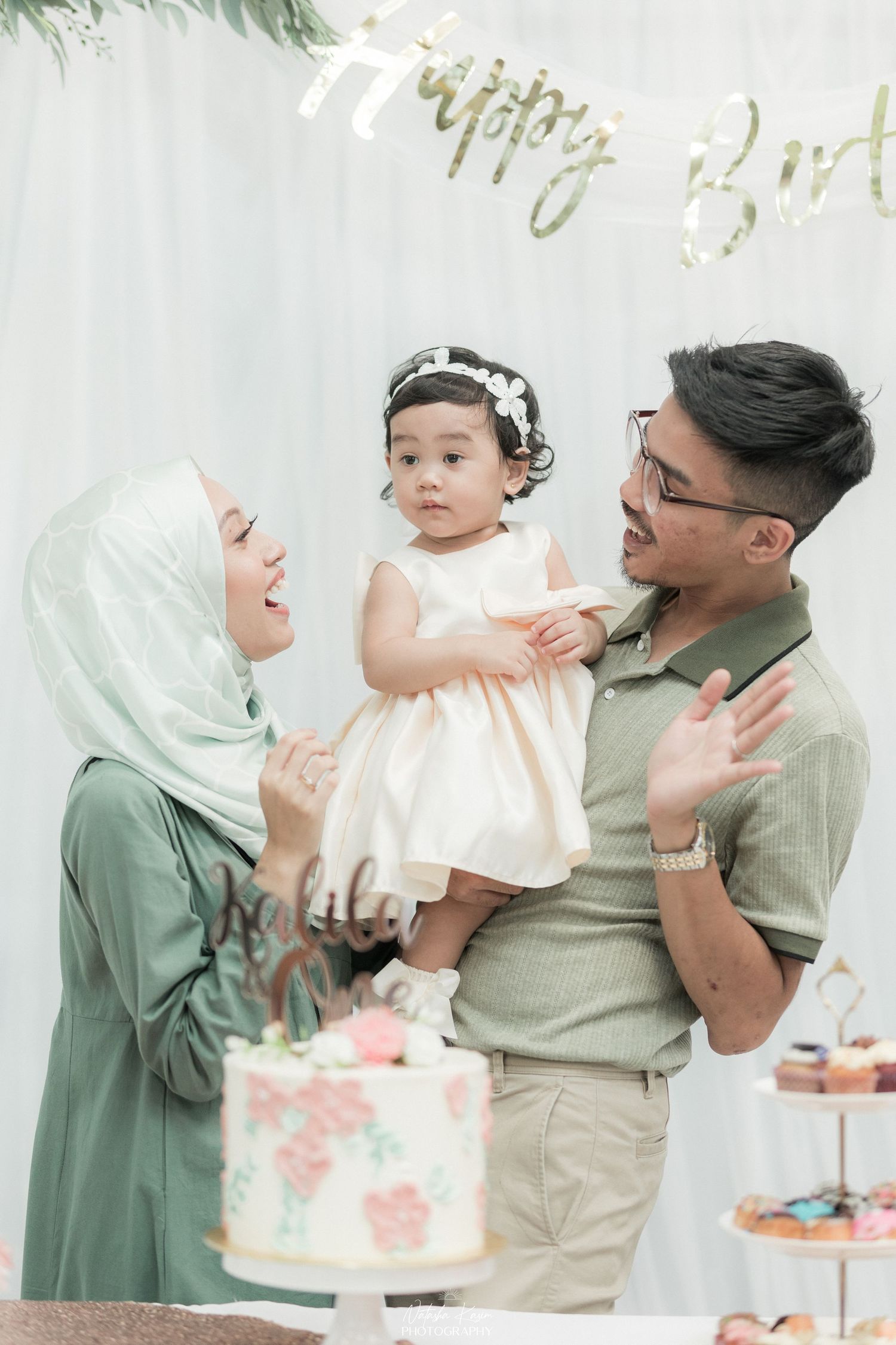 A family celebrates with a birthday cake against a white backdrop during a festive photoshoot.