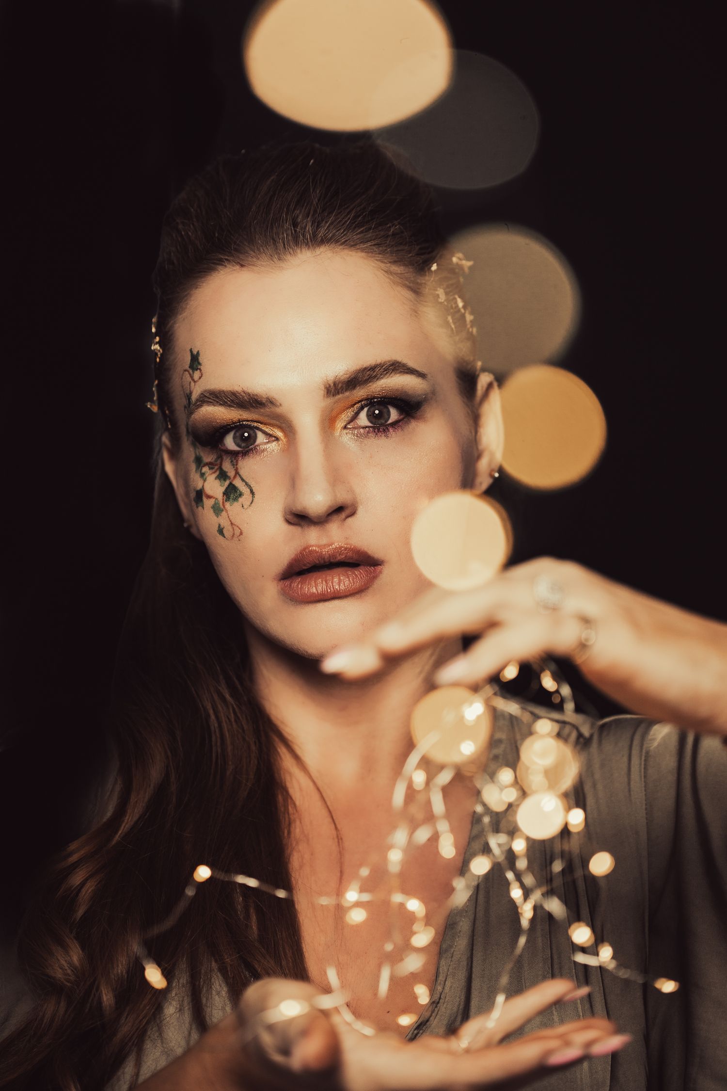 Artistic portrait with bokeh lights and decorative face elements in moody lighting.