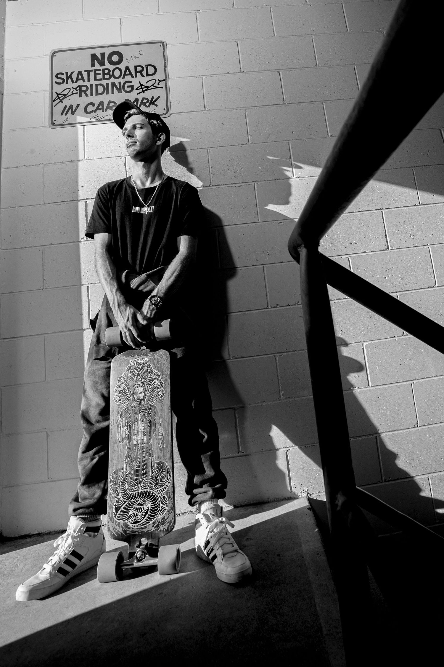 Black and white photo of a skateboarder standing defiantly under a 'No Skateboarding' sign.