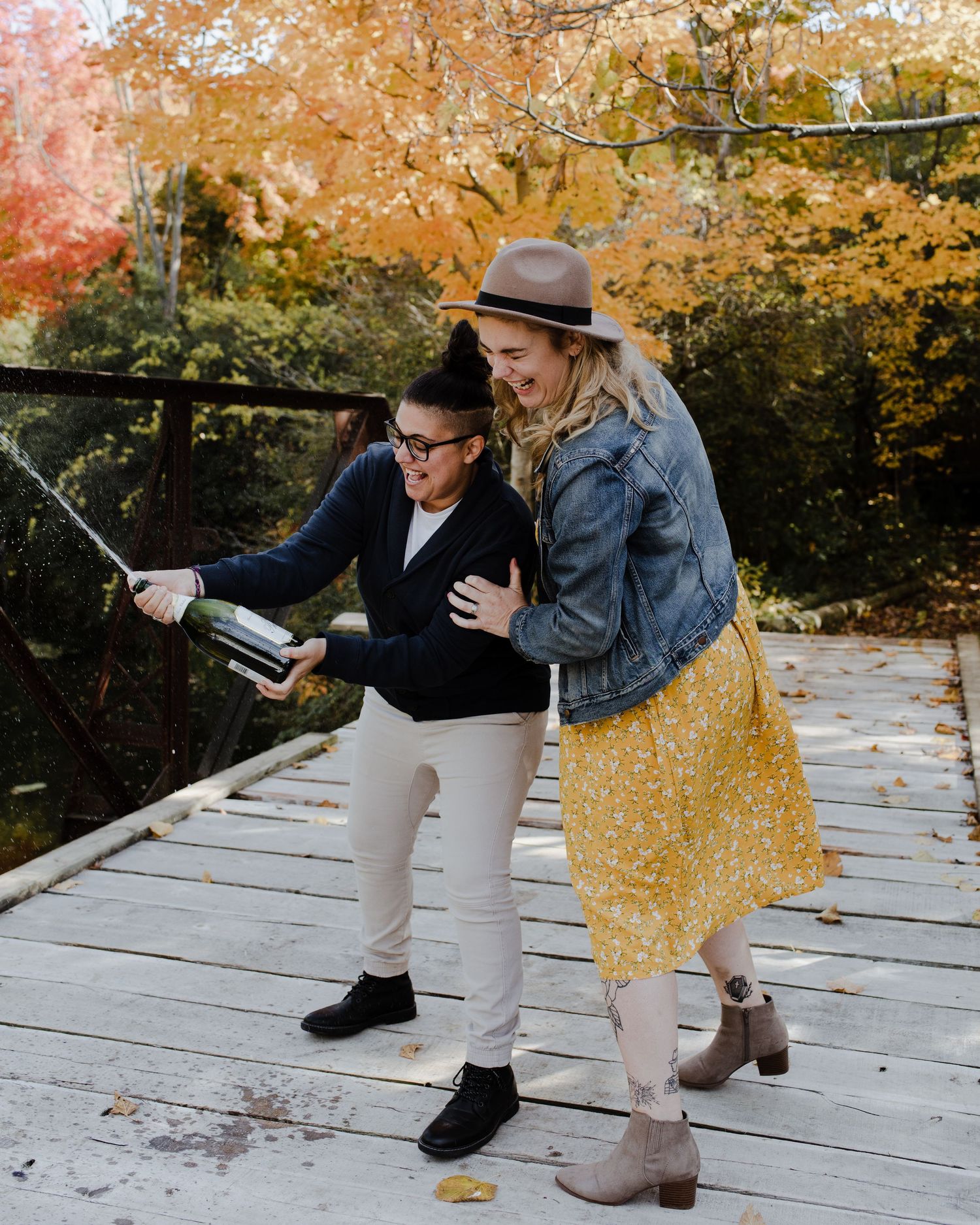 Mixed race lesbian couple laughs as they celebrate their engagement by popping a bottle of champagne which has exploded.