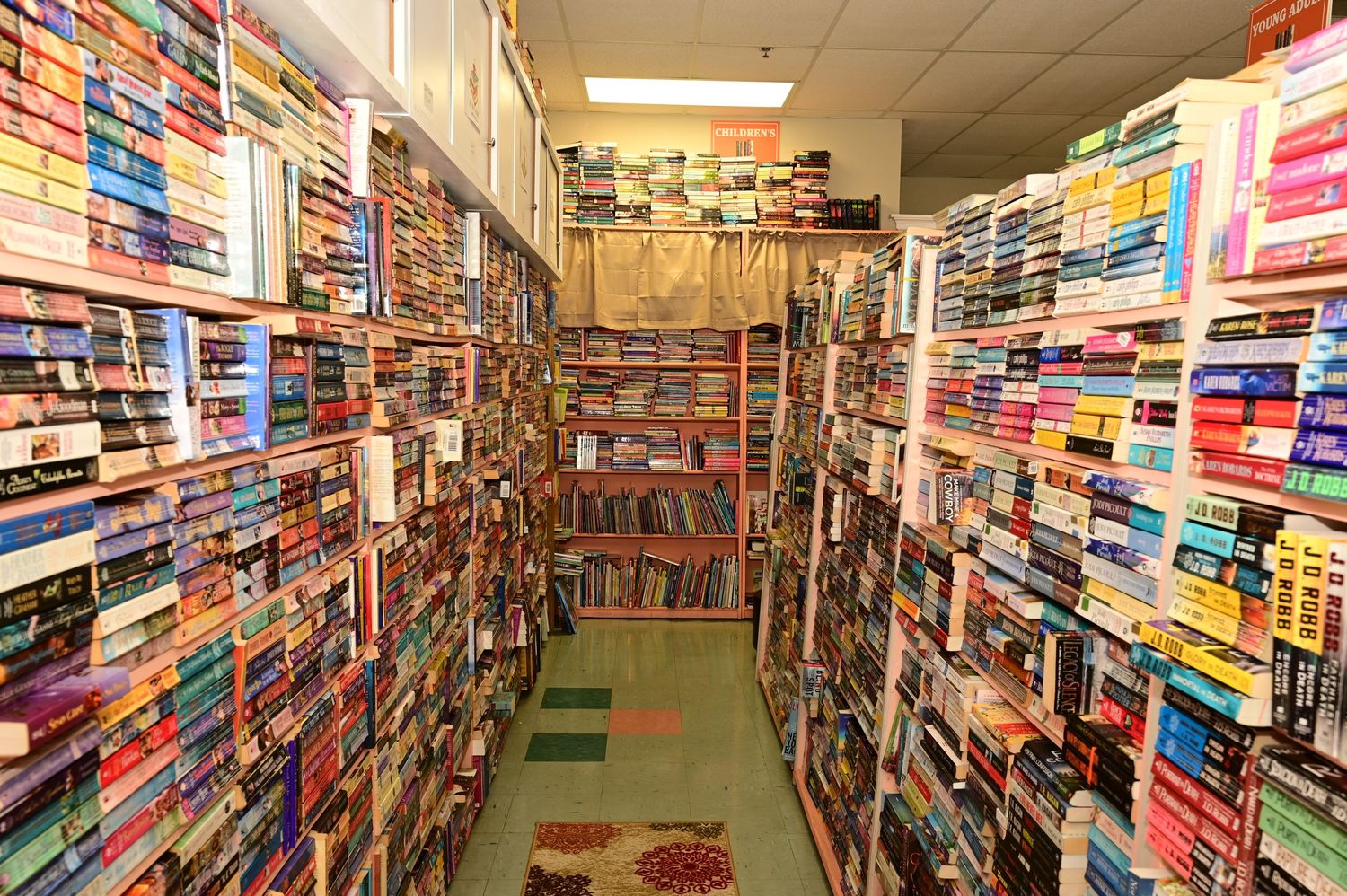 Narrow aisle between towering bookshelves filled with colorful book spines in used bookstore.