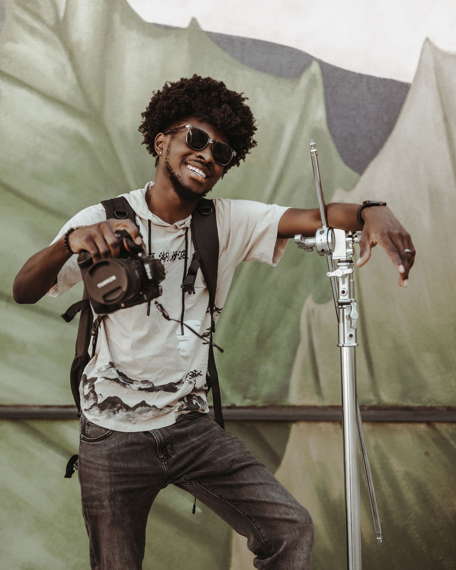 Photographer with camera and tripod smiling while working outdoors near festival tents.
