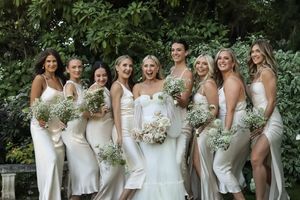 Cora Emilie Media Elegant wedding party gathers for group photos in white attire surrounded by greenery.