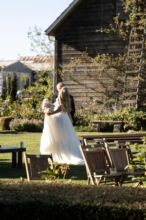 Cora Emilie Media Wedding couple shares intimate moment on rustic wooden benches at outdoor venue.