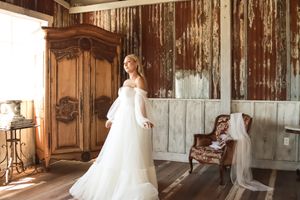 Cora Emilie Media A stunning wedding dress on display in a rustic setting with antique wooden furniture.