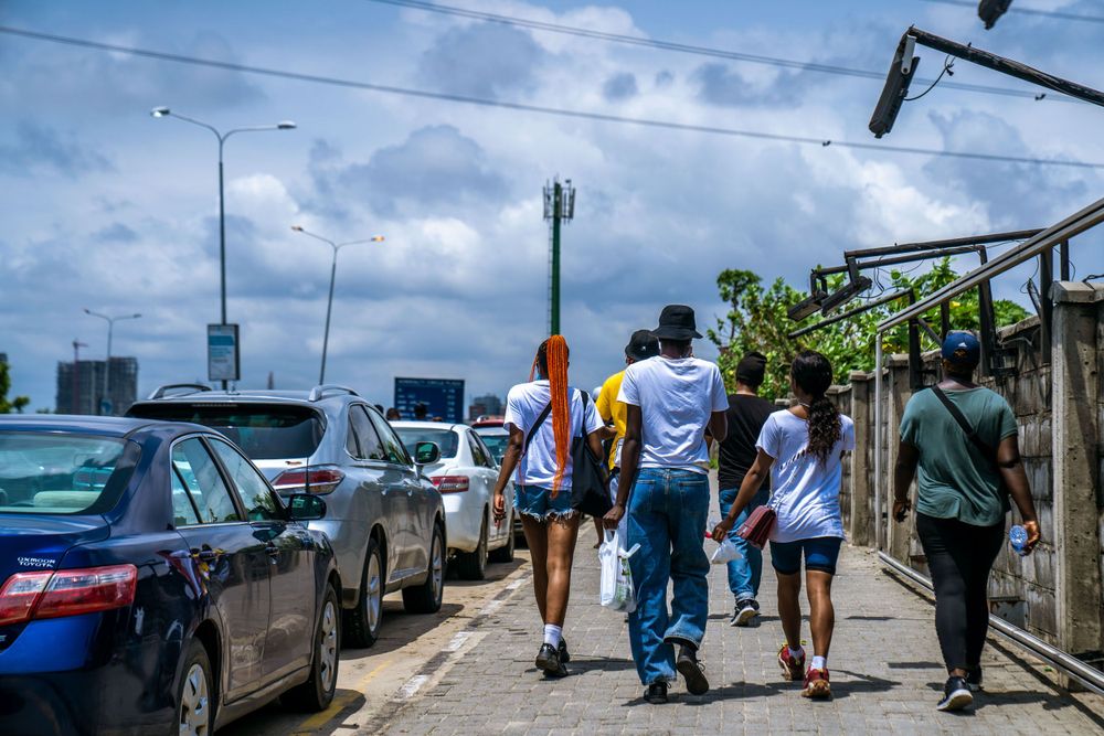 People walking along a waterfront promenade on a cloudy day with cars parked nearby.