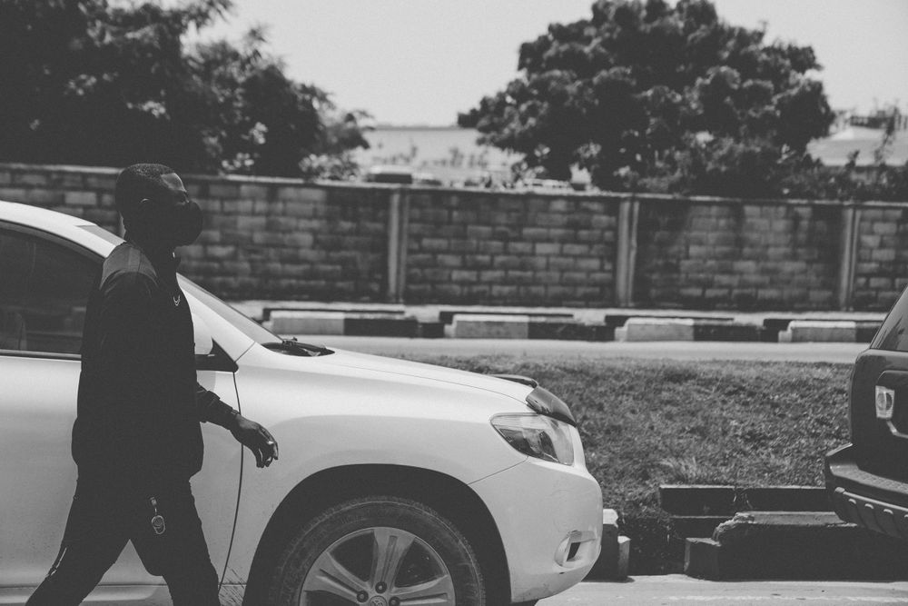 Black and white photo of parked cars with trees and a brick wall in the background.