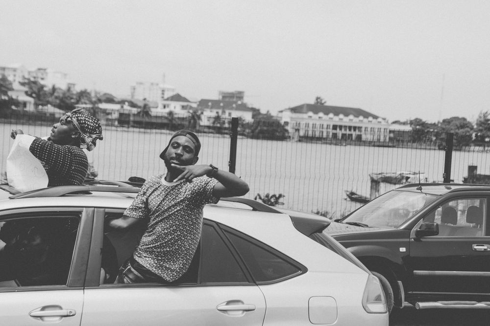 Black and white photograph of people interacting near parked vehicles in an urban setting.