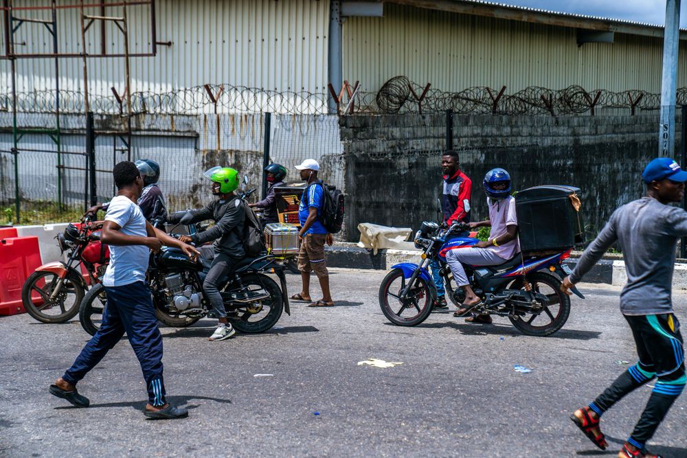 Motorcycles parked along a concrete wall with people gathered nearby.