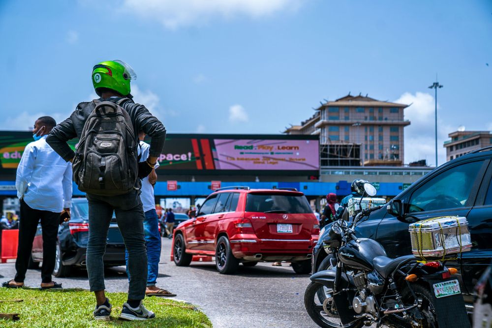 Cars and motorcycles parked in an outdoor lot with people walking around under blue skies.