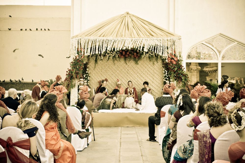 Wedding reception setup under an elegant tent with floral decorations and gathered guests.