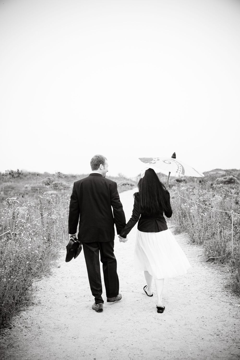 Black and white photo of couple walking hand in hand down a rustic path.
