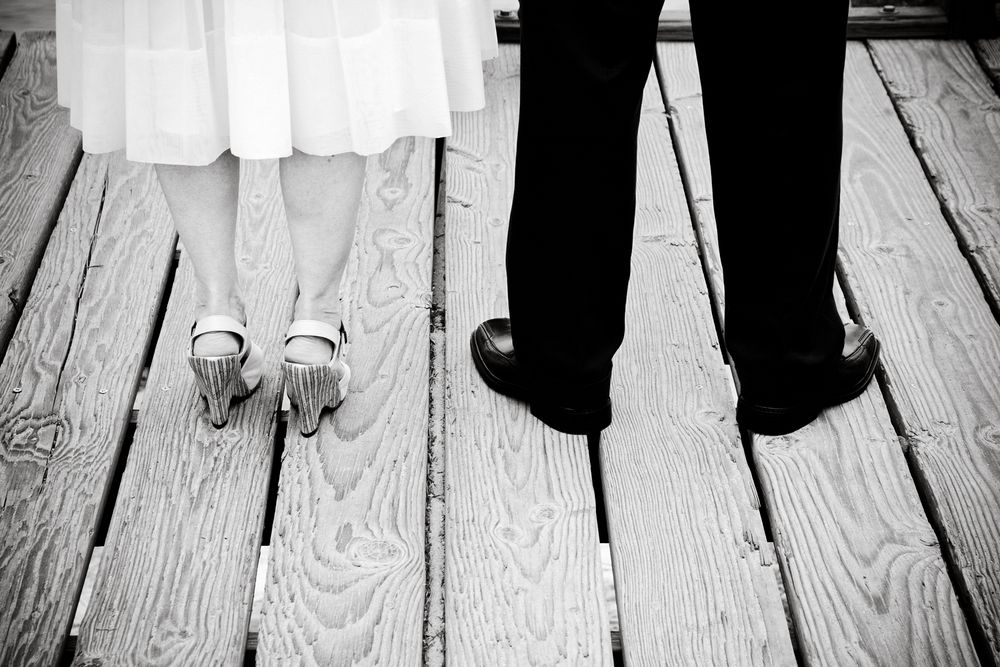 Artistic black and white photo of feet on wooden deck boards showing formal and casual shoes.