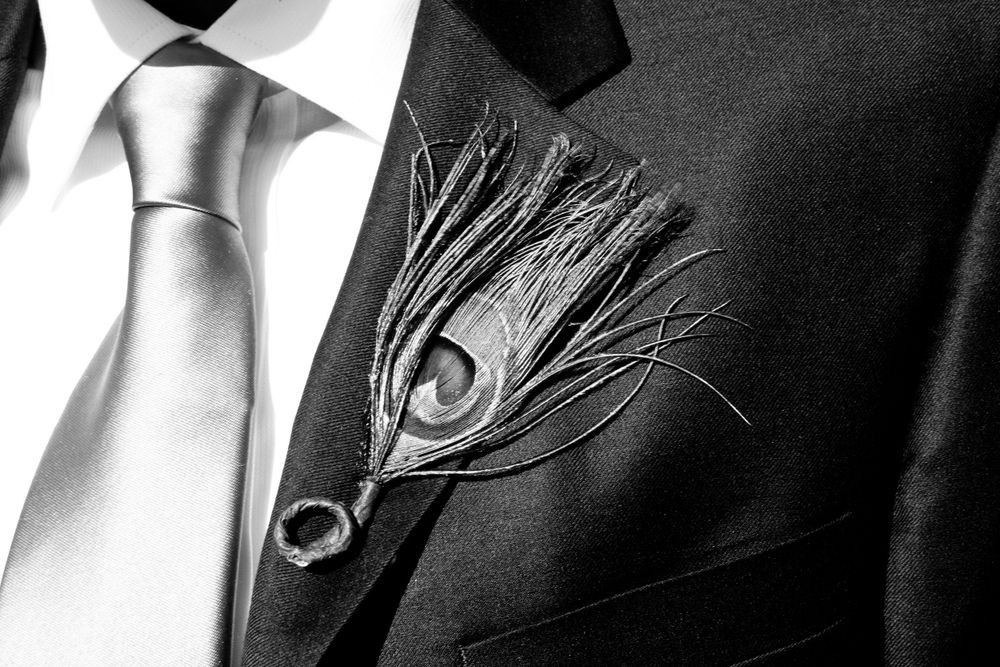 Close-up of peacock feather boutonniere on black suit jacket with silver tie.