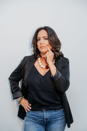 Stylish woman in black blazer and jeans strikes thoughtful pose against white background.