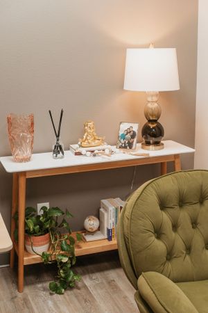 Console table styled with lamp, decor items and green tufted chair.