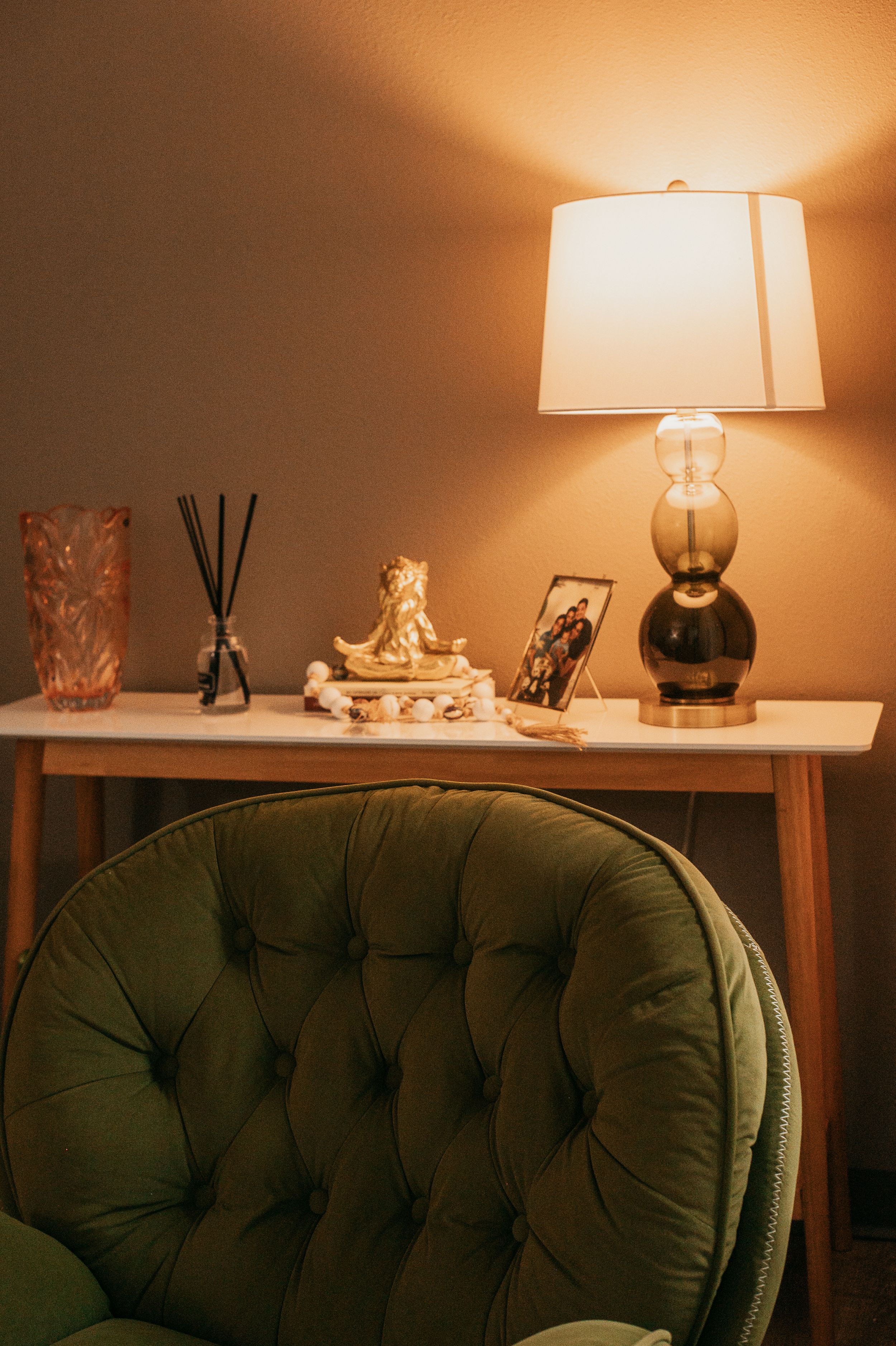 Warm-lit vignette of console table with decorative items and olive green chair.