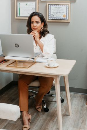Business professional working at modern desk with laptop and framed certificates on wall.