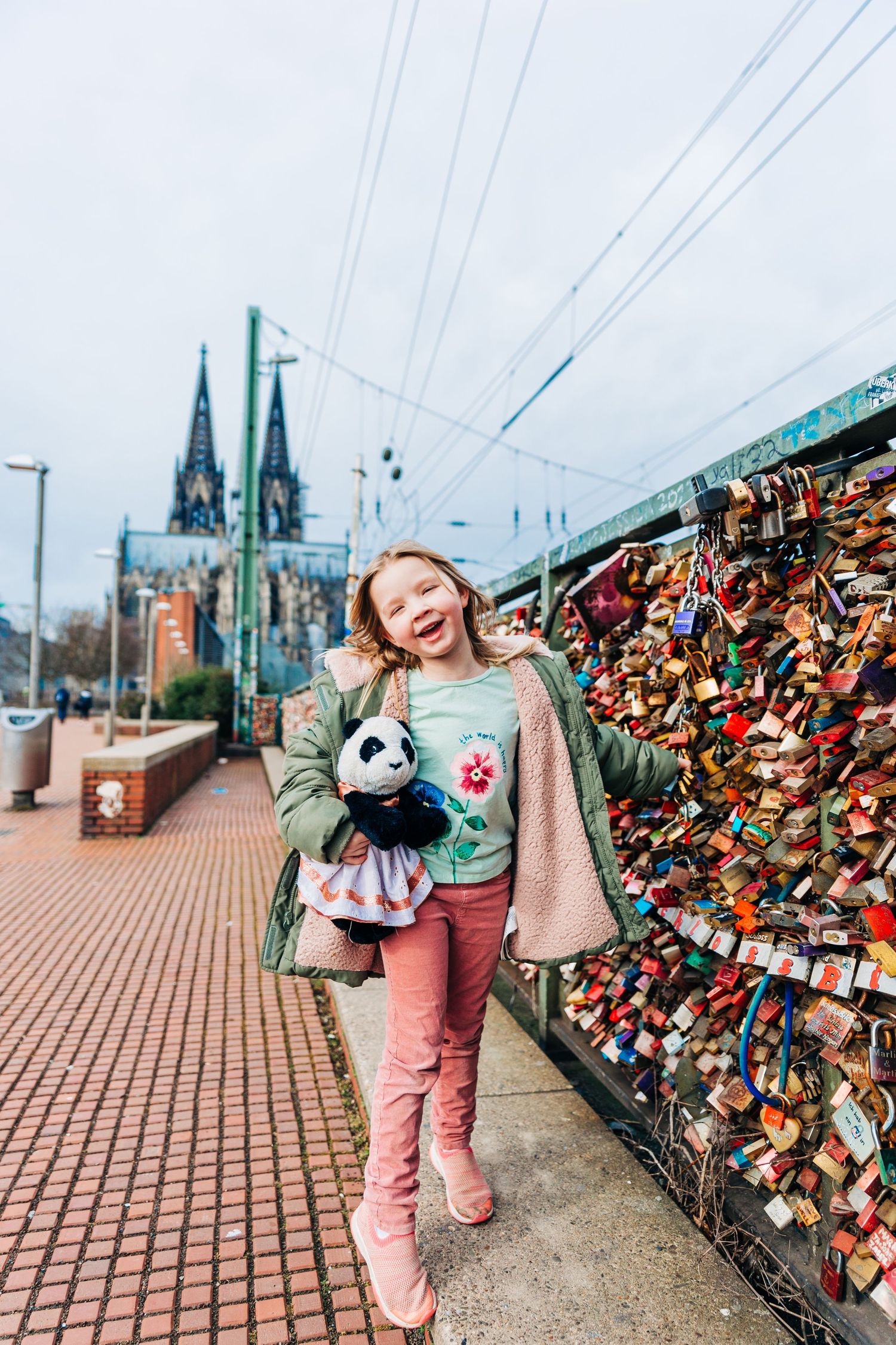 A winter scene by a love locks bridge in Cologne with the cathedral spires visible in the background.