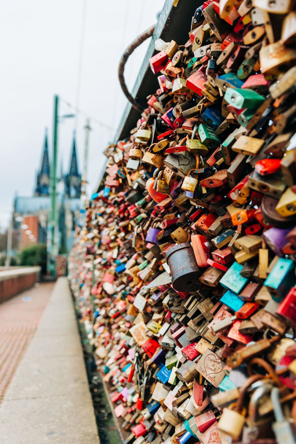 Thousands of colorful love locks on bridge railing with Cologne Cathedral spires in background.