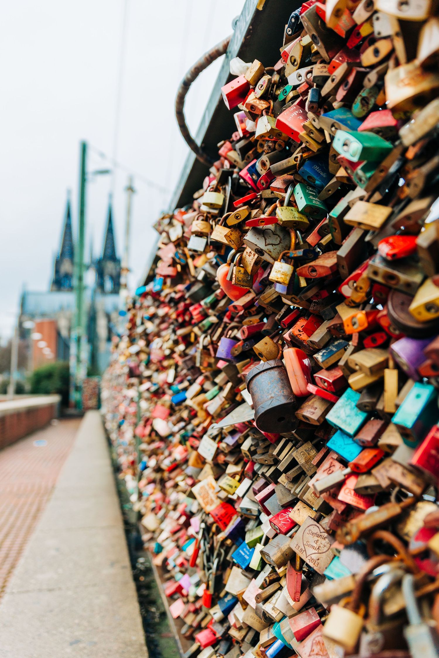 Thousands of colorful love locks on bridge railing with Cologne Cathedral spires in background.
