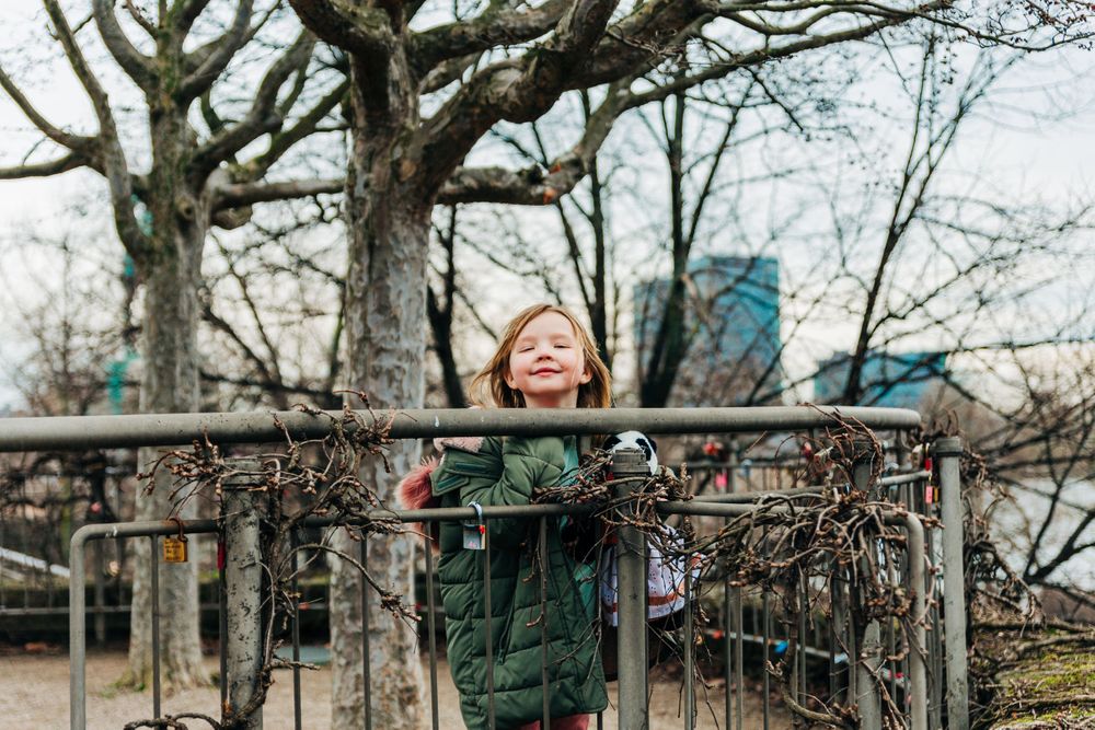 Winter scene at a playground with bare trees and urban buildings in background.