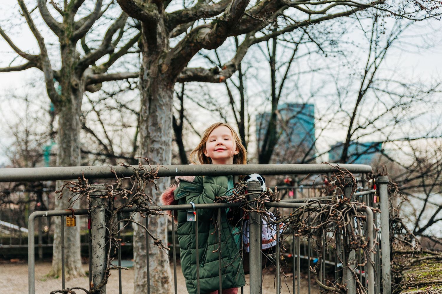 Winter scene at a playground with bare trees and urban buildings in background.