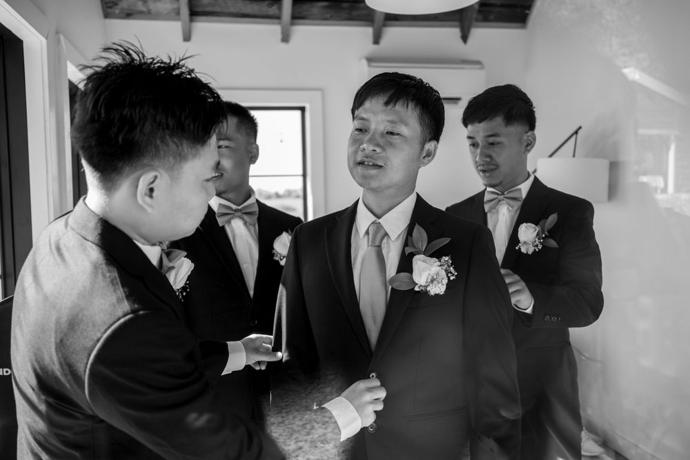 Groomsmen in suits with boutonnieres helping the groom prepare before the wedding ceremony.