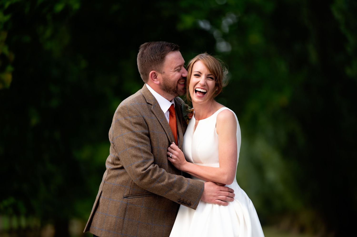 Happy newlyweds share joyful moment together in lush garden setting.