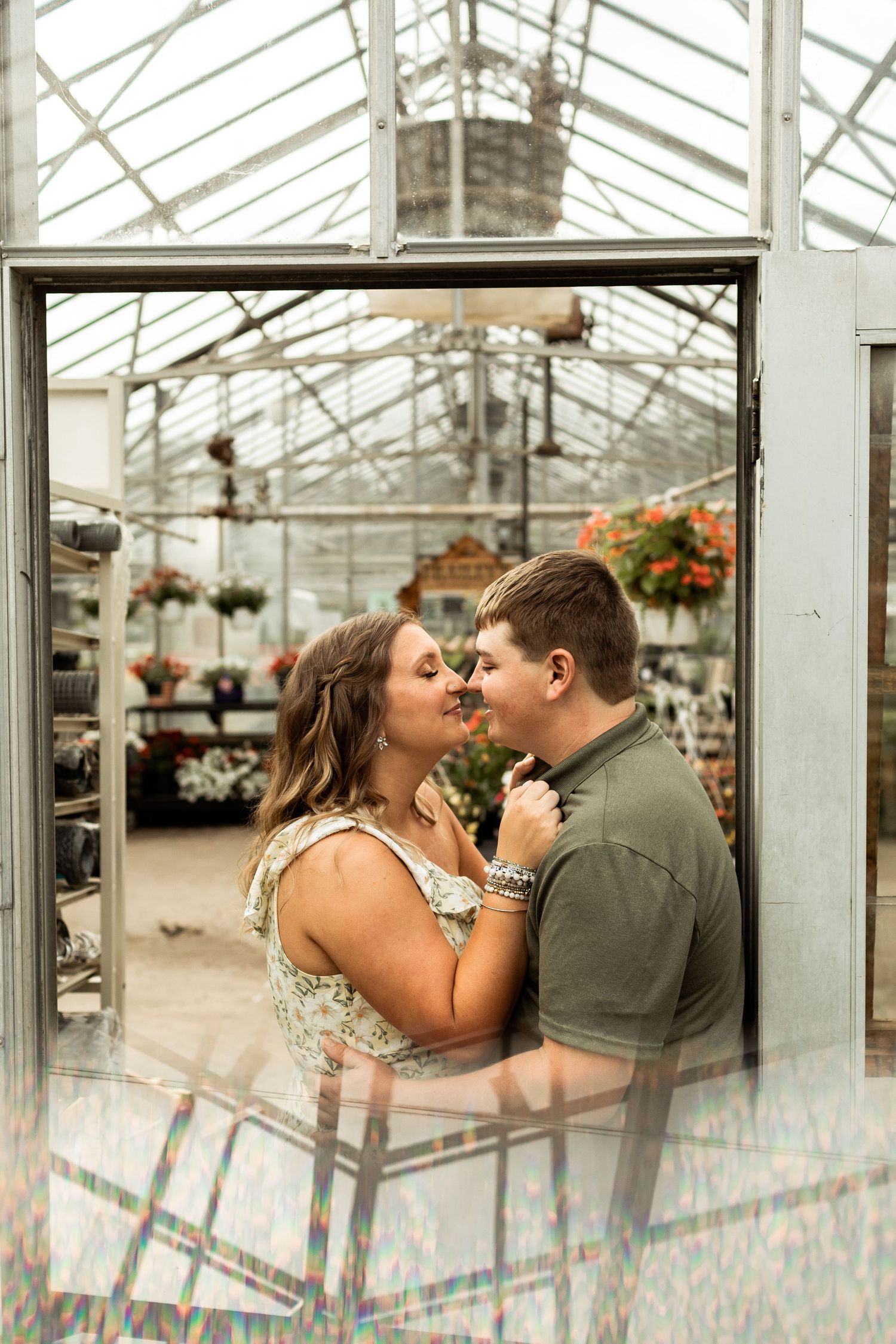 Couple sharing romantic moment in greenhouse surrounded by hanging plants and flowers.
