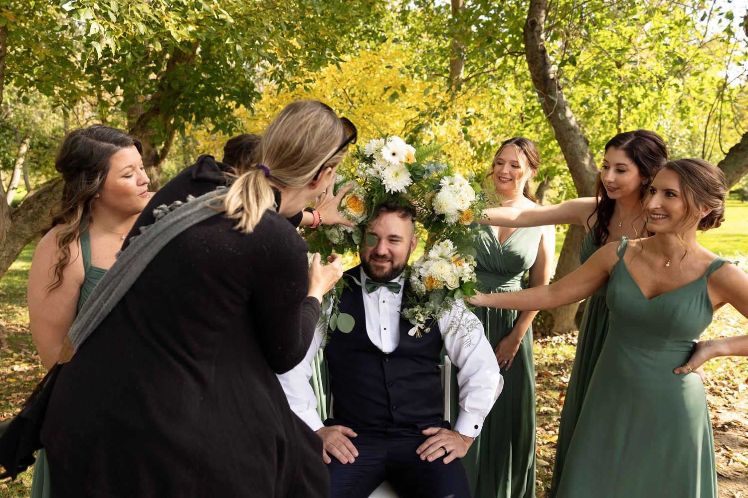 Wedding party members laugh and celebrate together in a scenic outdoor autumn setting.