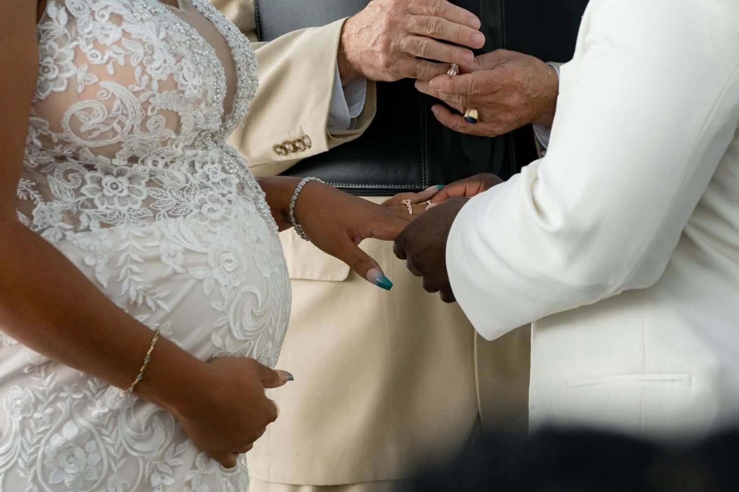 Close-up view of hands during a wedding ceremony as rings are exchanged against a backdrop of white lace.
