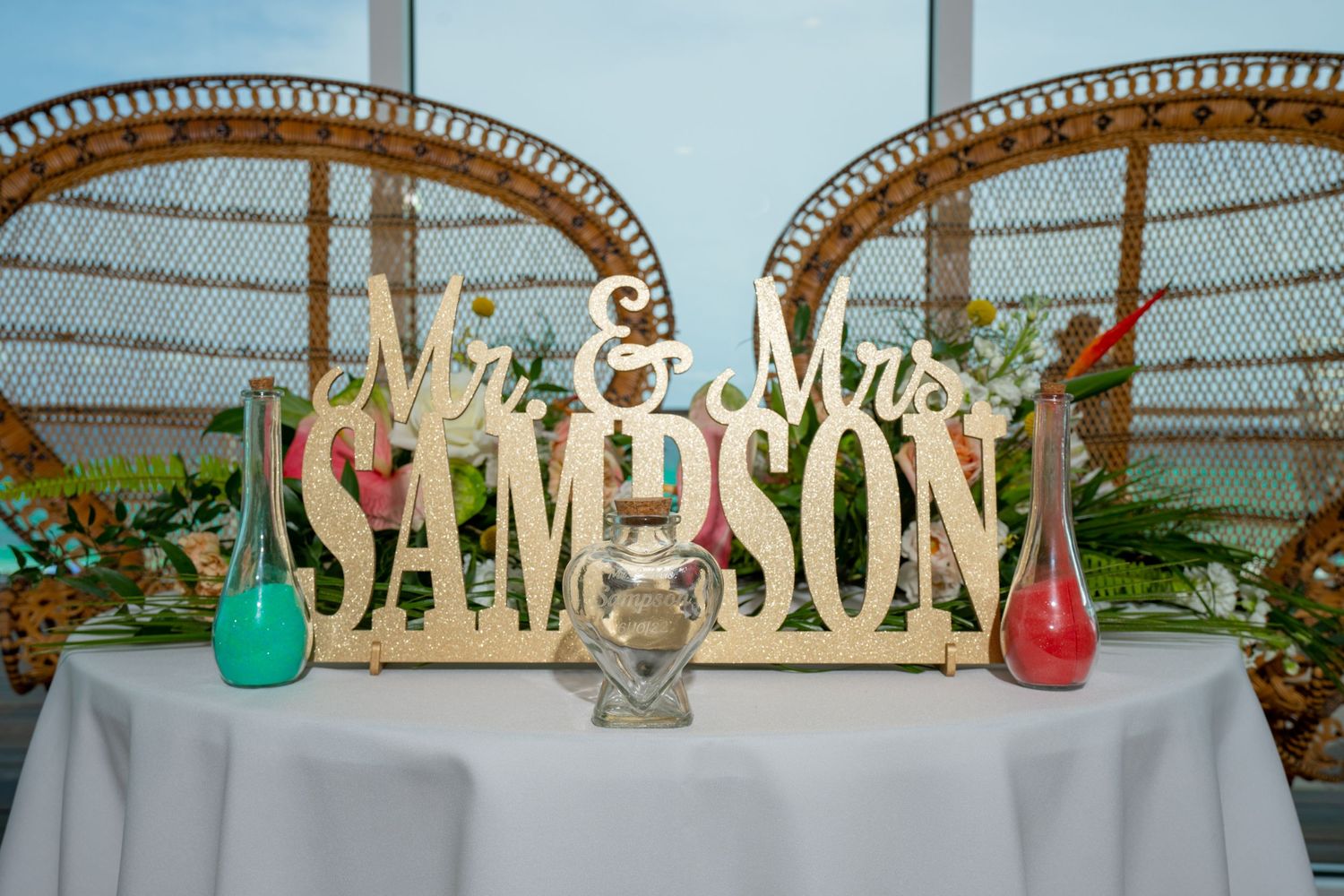 A wooden Mr. & Mrs. sign on a table with a white tablecloth and colorful glass vases, set against an arched structure.