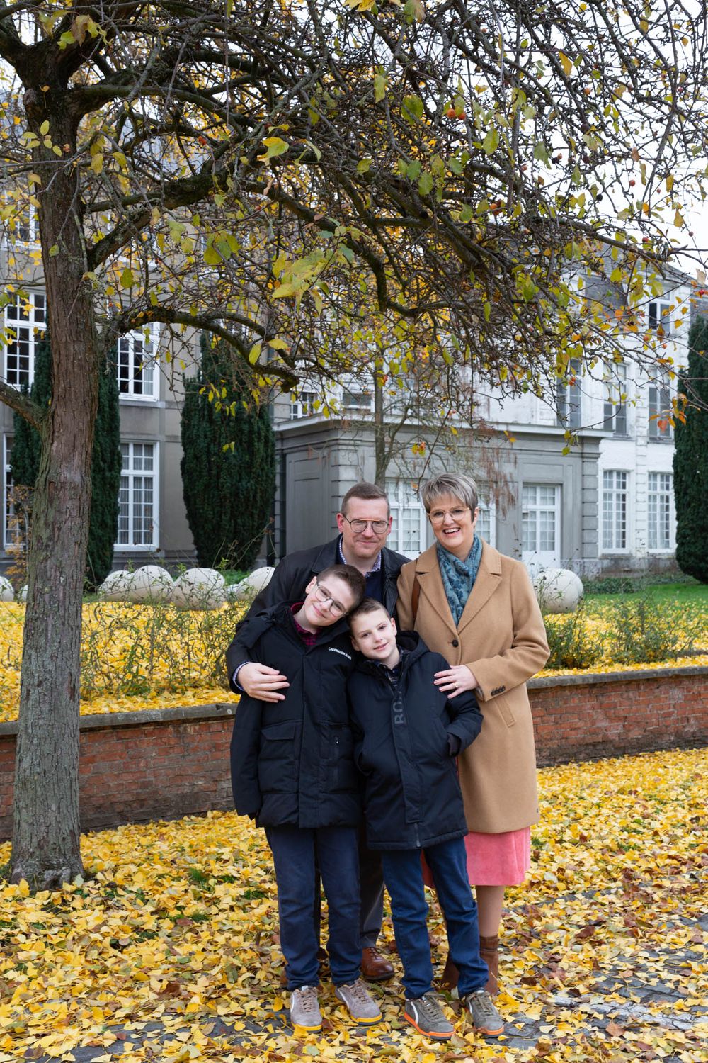 A family poses together on an autumn day with yellow leaves and a grand building in the background.